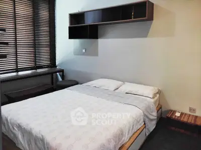 Cozy bedroom with modern furnishings and natural light from large window blinds.