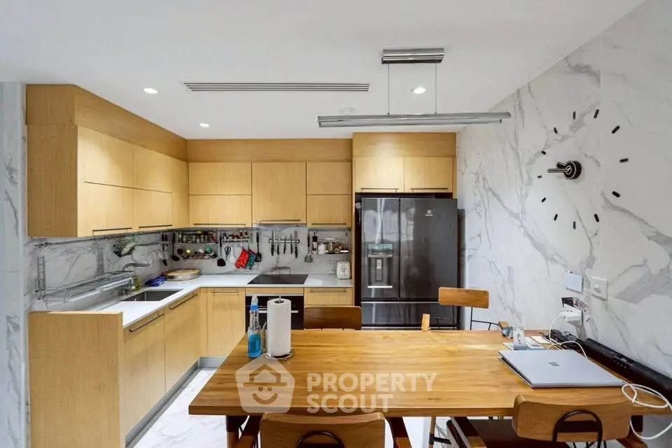 Modern kitchen with wooden cabinets, marble backsplash, and dining table, featuring a sleek black fridge.