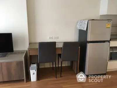 Modern apartment interior with fridge, TV, and dining area on wooden flooring.