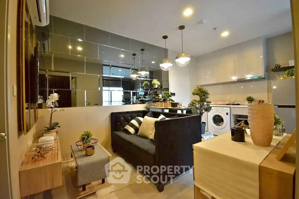 Modern living room with stylish decor and open kitchen layout, featuring a washing machine and elegant lighting.