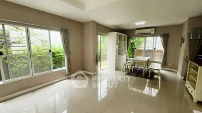 Spacious living room with large windows and garden view, featuring modern furniture and air conditioning.