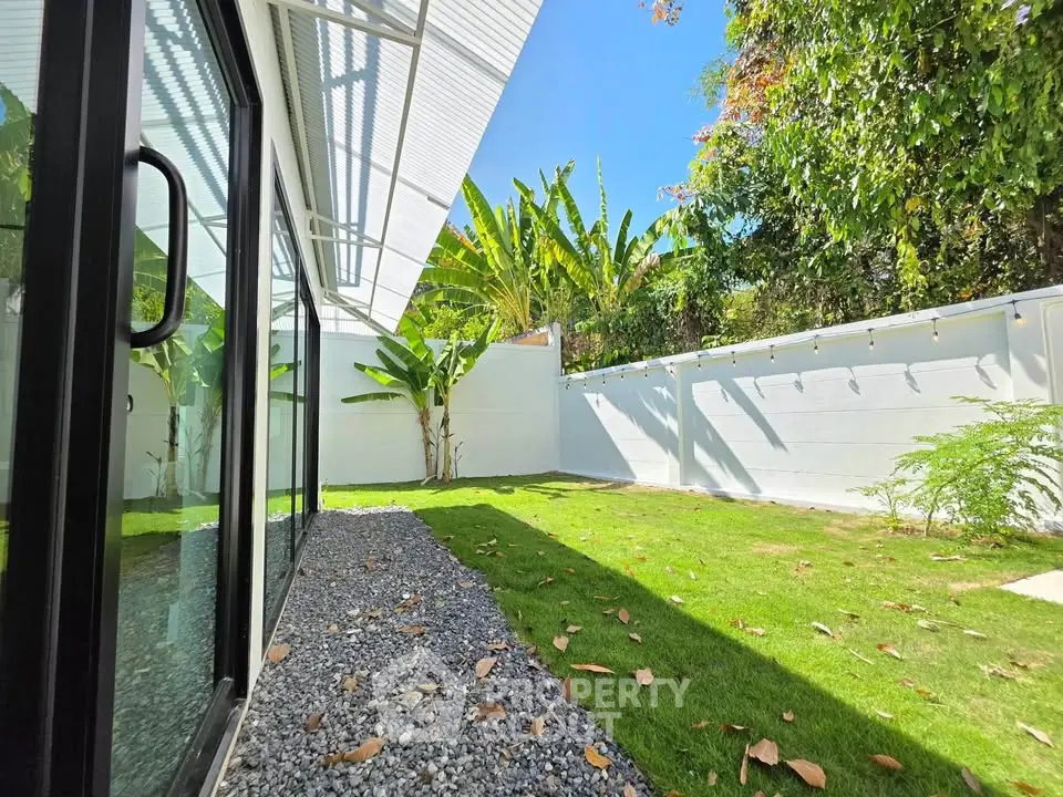 Spacious backyard with lush greenery and modern glass sliding doors, perfect for outdoor relaxation.