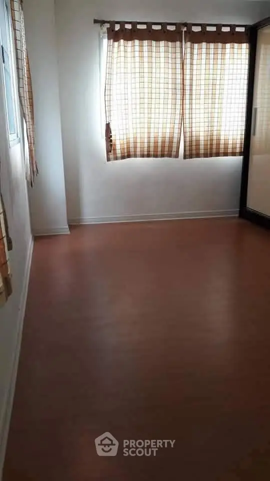 Spacious empty room with wooden flooring and large windows with curtains.