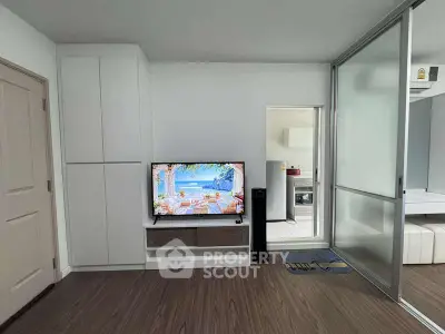 Modern living room with sleek design and TV, adjacent to kitchen area.