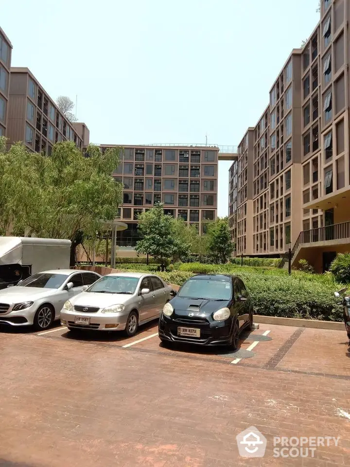 Modern apartment complex with parking and lush greenery in urban setting.