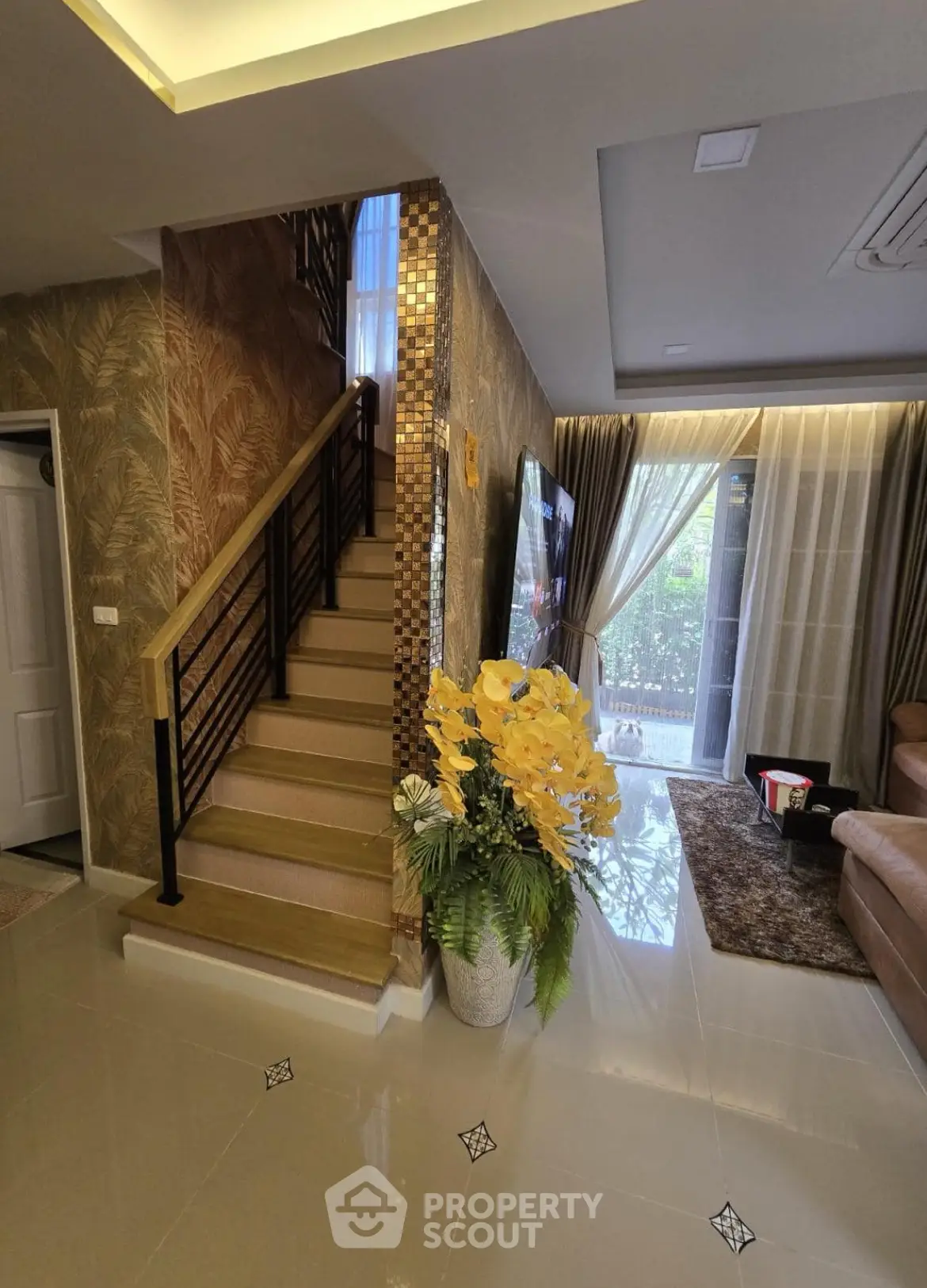Elegant living room with staircase, modern decor, and large windows for natural light.