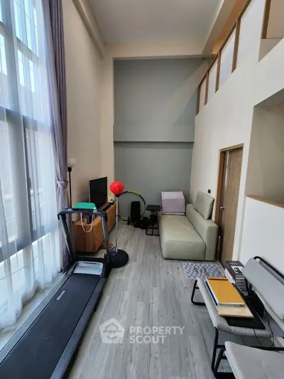 Modern living room with high ceilings and treadmill, featuring large windows and stylish decor.