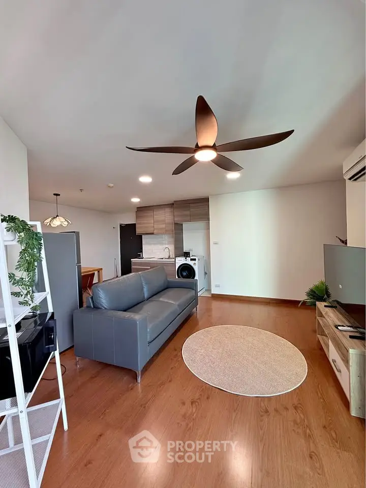 Modern living room with sleek furniture and ceiling fan, open kitchen layout, and wooden flooring.