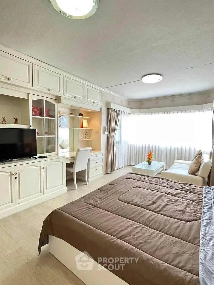 Spacious bedroom with elegant decor and natural light, featuring a cozy seating area and modern furnishings.