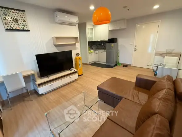 Modern living room with open kitchen, featuring brown leather sofa and glass coffee table.