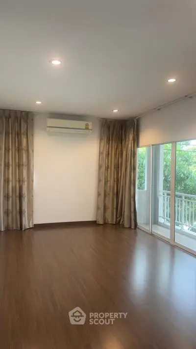 Spacious empty room with hardwood floors and large windows overlooking greenery.