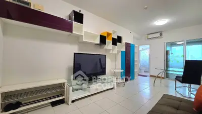 Modern living room with sleek TV unit and colorful shelving, adjacent to a bright bathroom.