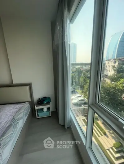 Modern bedroom with large windows offering a city view, featuring sleek design and natural light.