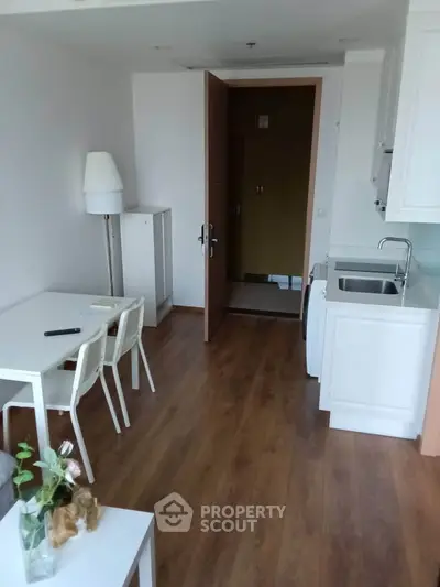 Modern apartment interior with wooden flooring, white furniture, and a compact kitchen area.