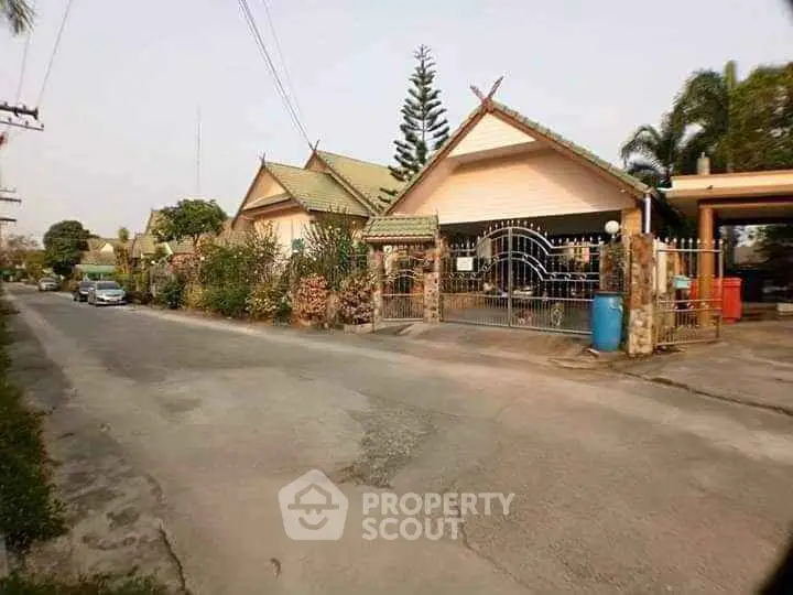Charming suburban house with gated entrance and lush greenery on a quiet street.