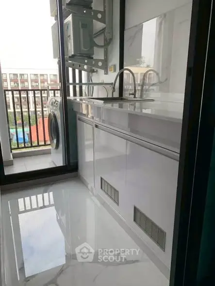 Modern kitchen with sleek white cabinetry and balcony view, featuring a washing machine and dual sinks.