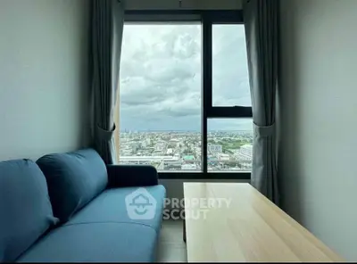 Modern living room with stunning city view through large window, featuring a cozy blue sofa and wooden table.