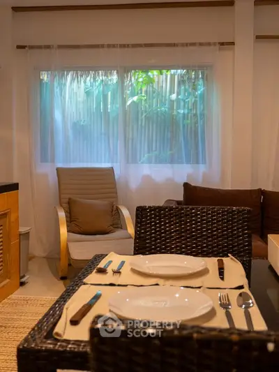 Cozy living room with dining area, featuring elegant wicker chairs and a serene garden view through the window.