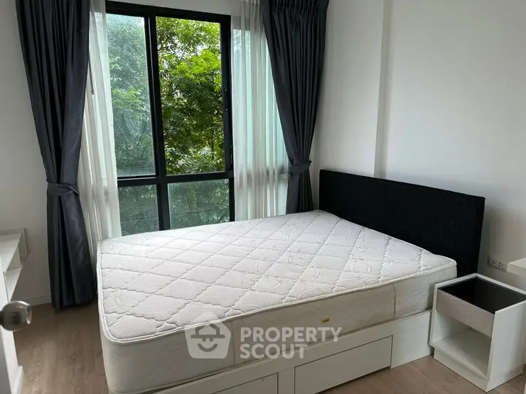 Cozy bedroom with large window and lush green view, featuring a comfortable bed and modern decor.