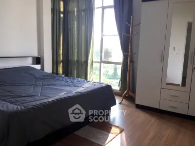 Spacious bedroom with large window and modern furnishings, offering ample natural light and a serene atmosphere.