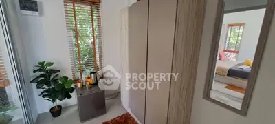 Cozy bedroom with wardrobe, mini fridge, and lush greenery view.