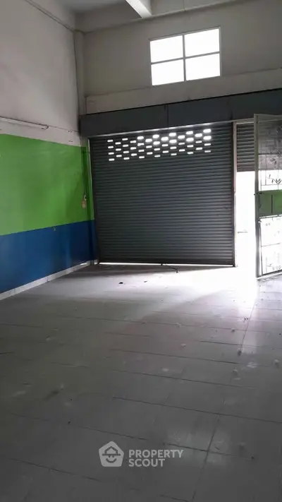 Spacious commercial space with high ceiling and large shutter door, ideal for retail or storage.