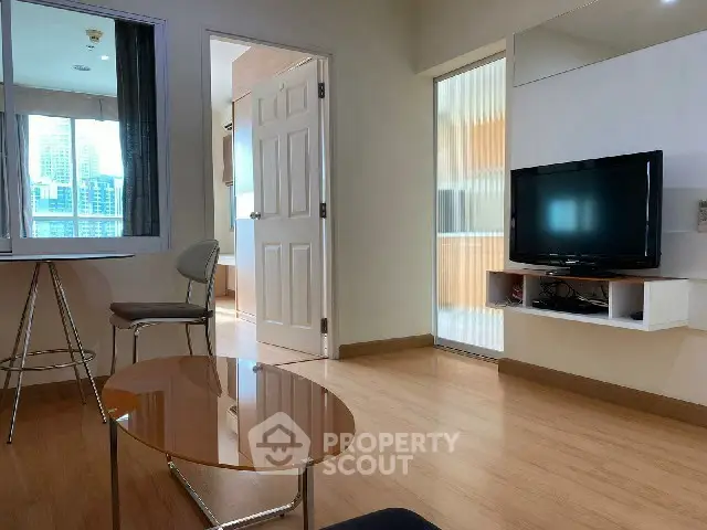 Modern living room with sleek wooden flooring and large TV, featuring a bright window view.
