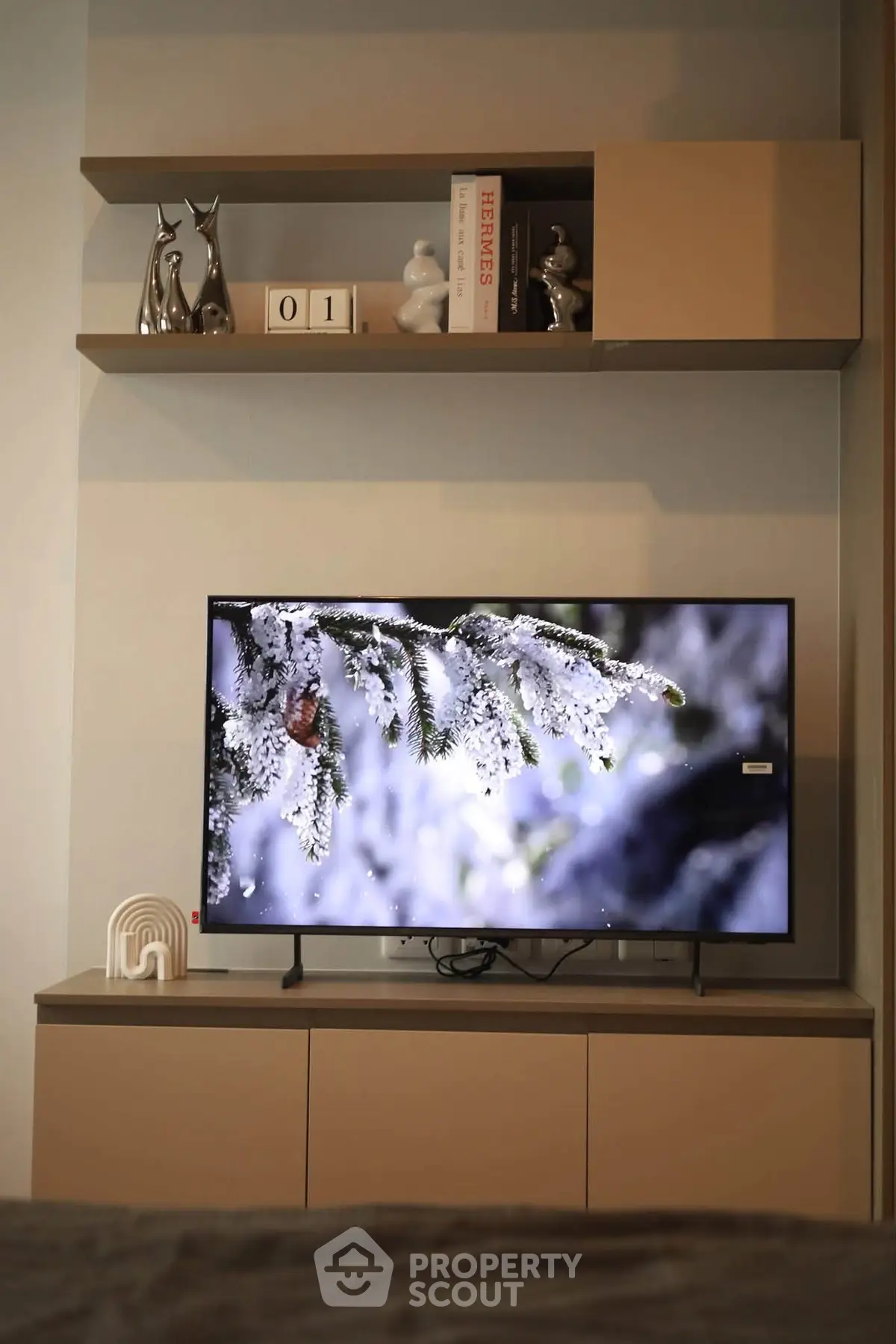 Modern living room with stylish shelves and flat-screen TV displaying winter scene.