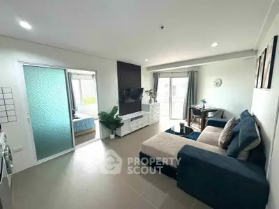 Modern living room with stylish furniture and sliding door to bedroom, featuring natural light and contemporary decor.