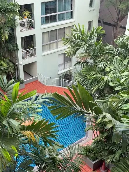 Lush tropical pool area in modern apartment complex with palm trees and vibrant blue water.