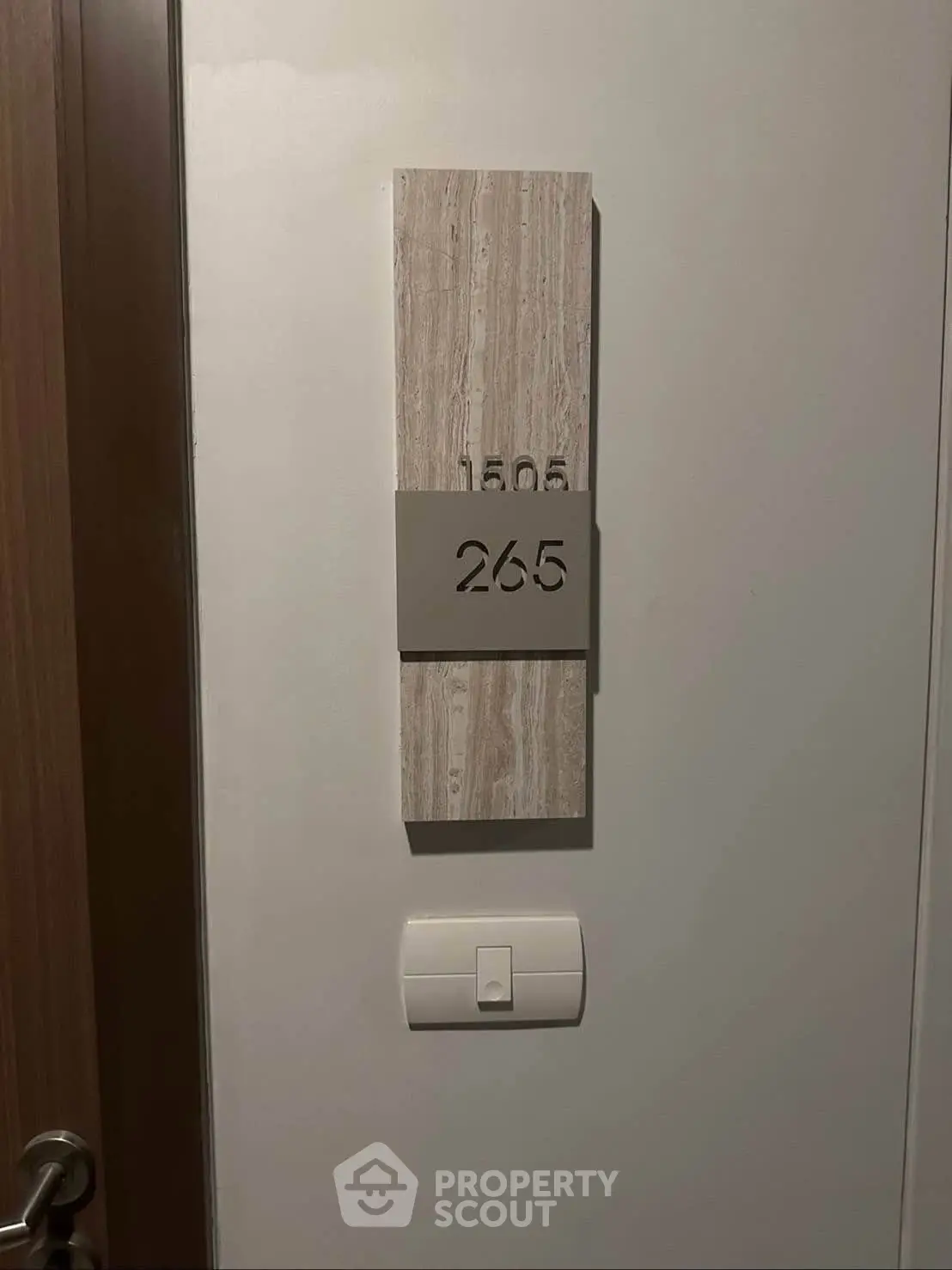 Modern apartment door with sleek room number plaque and light switch, showcasing contemporary design.