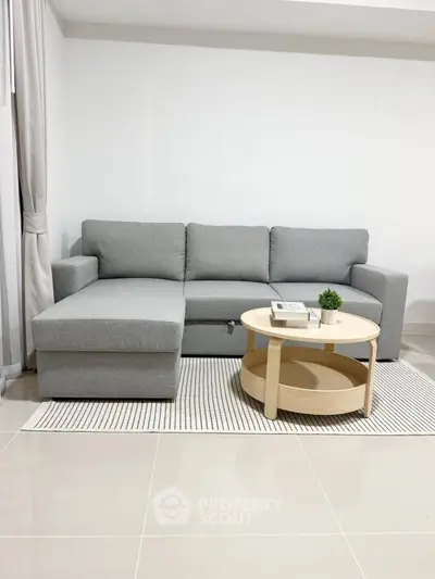 Modern living room with stylish gray sofa and round wooden coffee table on a sleek tiled floor.