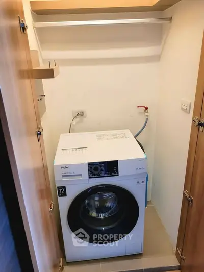 Compact laundry area with modern washing machine in a cozy storage space.