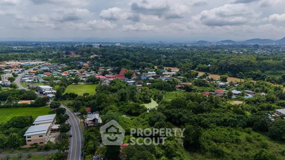 Scenic aerial view of lush green landscape and residential area with distant mountains.