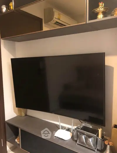 Modern living room with wall-mounted TV and sleek storage unit, featuring contemporary decor and air conditioning.