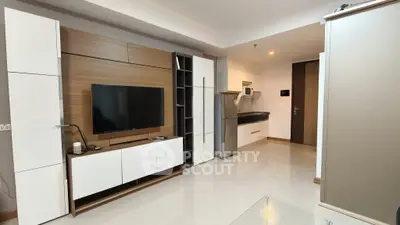 Modern living room with sleek TV unit and compact kitchen area in stylish apartment.