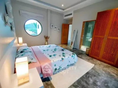 Spacious bedroom with modern decor and unique circular window, featuring stylish furniture and ample natural light.