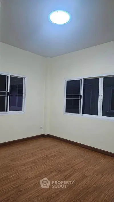 Spacious empty room with wooden flooring and large windows, perfect for customization.