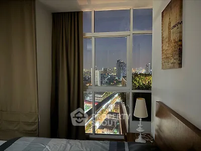 Cozy bedroom with large windows offering a stunning city view, complemented by warm lighting and tasteful decor, perfect for urban living.