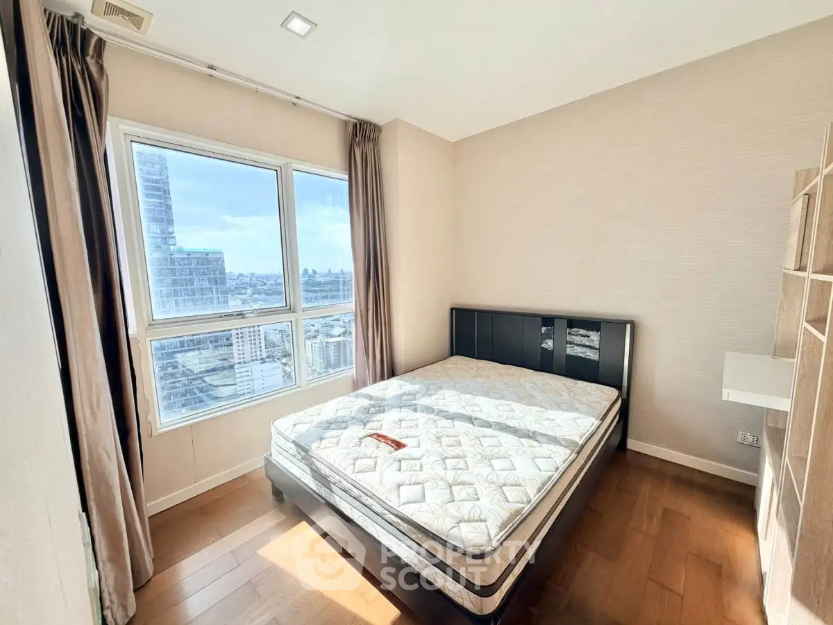 Bright bedroom with large window and city view, featuring a comfortable bed and wooden flooring.