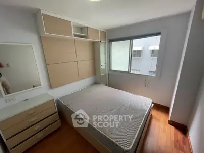 Cozy bedroom with wooden flooring and built-in storage, featuring a large window for natural light.