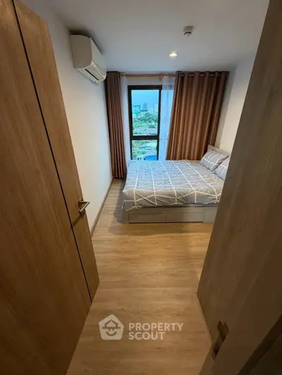 Cozy bedroom with modern decor and city view, featuring wooden flooring and air conditioning.