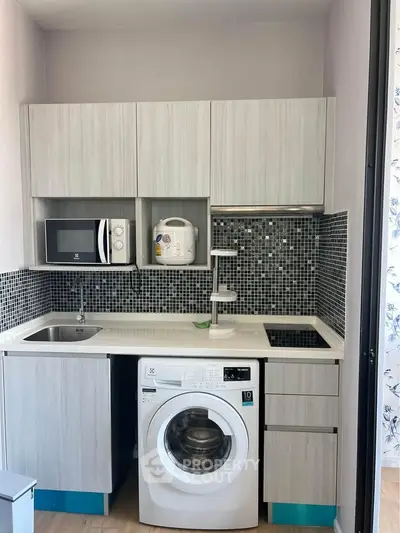 Modern compact kitchen with washing machine and microwave, sleek cabinetry and stylish backsplash.
