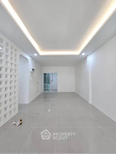 Spacious modern living room with sleek tile flooring and ambient ceiling lighting.