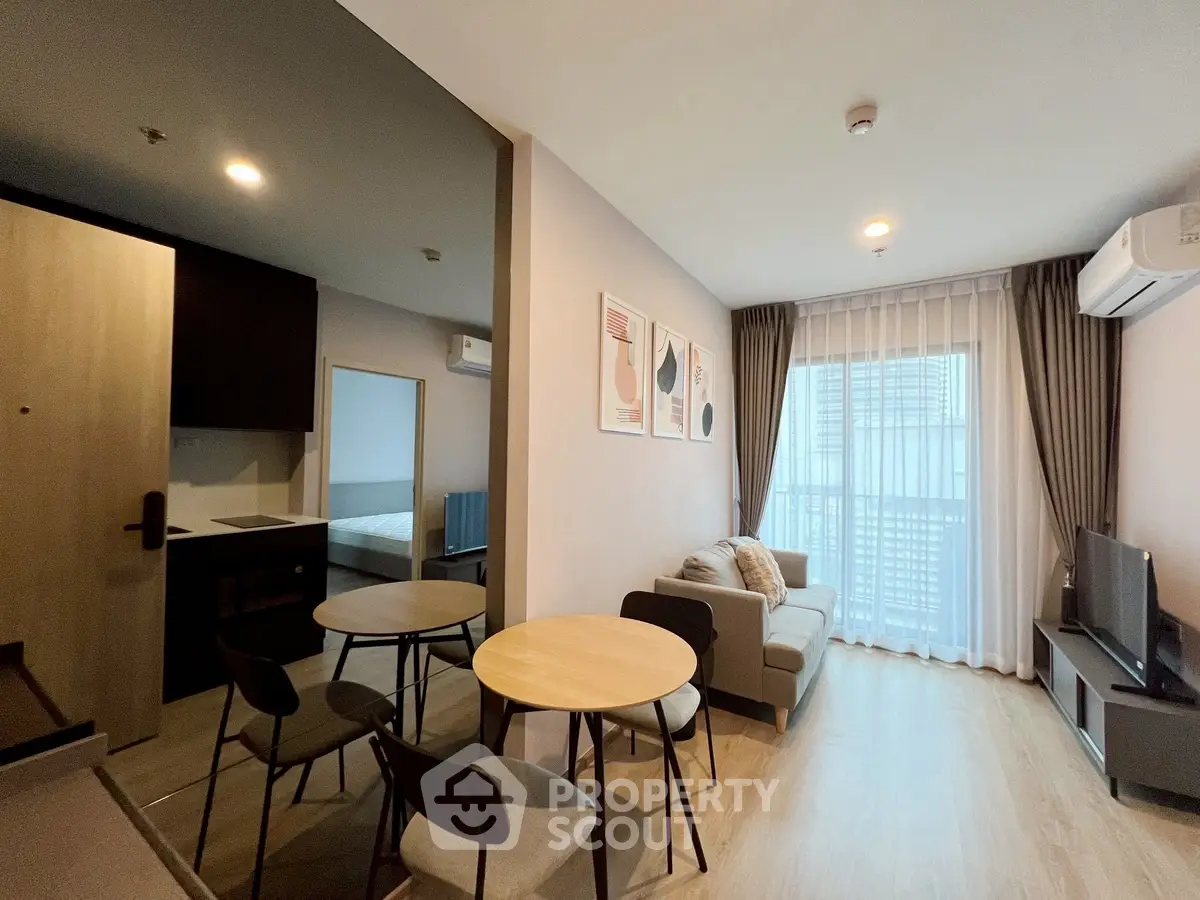 Modern living room with open kitchen and natural light, featuring stylish decor and cozy seating.