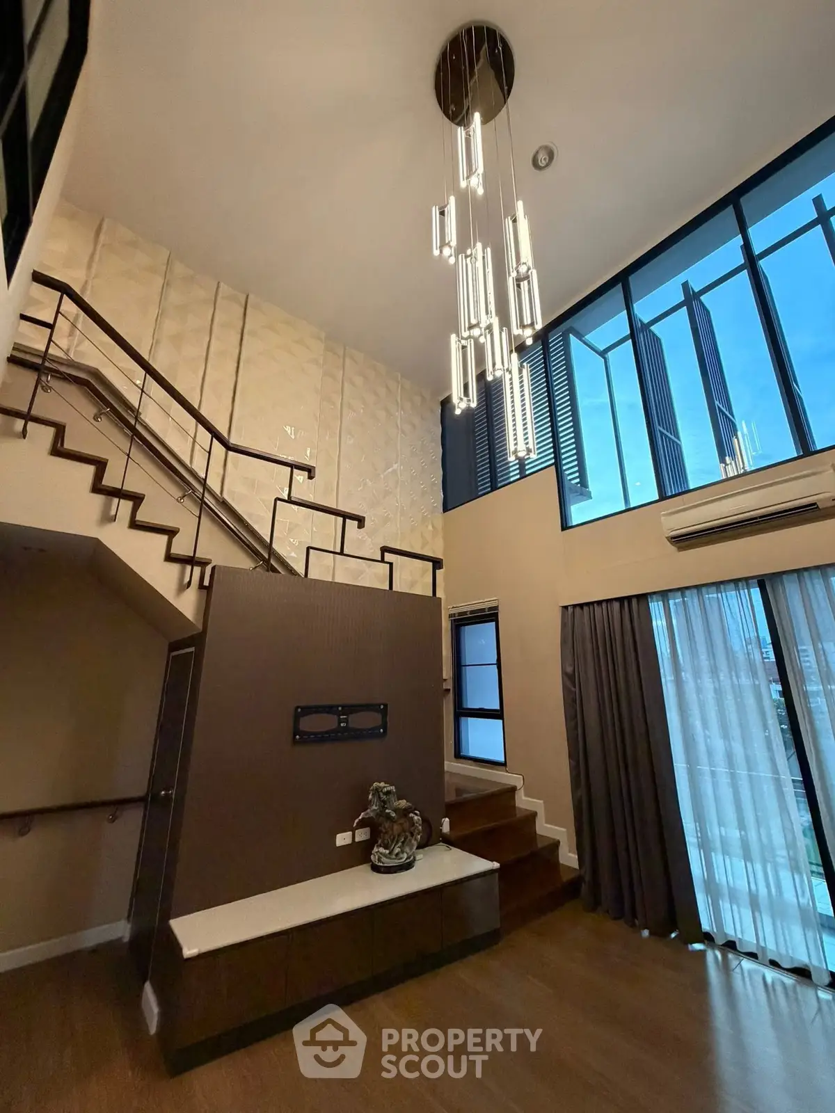 Luxurious modern living room with high ceilings and elegant staircase, featuring large windows and stylish lighting.