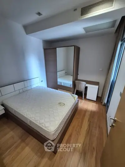 Modern bedroom with wooden flooring, mirrored wardrobe, and cozy desk area.