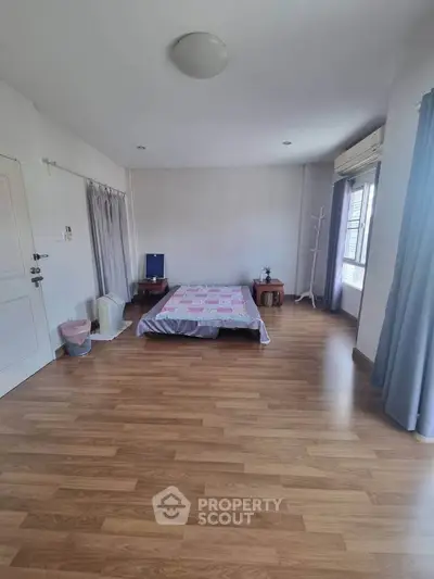 Spacious bedroom with wooden flooring and natural light, featuring minimalist decor and cozy ambiance.