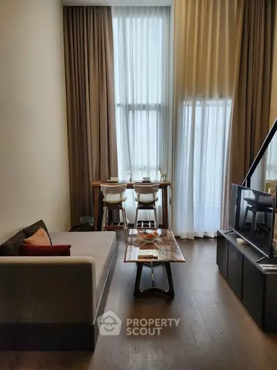 Modern living room with high ceilings and elegant decor, featuring a cozy sofa and dining area by tall windows.
