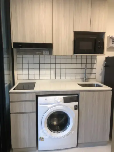 Modern compact kitchen with integrated washing machine and microwave, featuring sleek cabinetry and tiled backsplash.